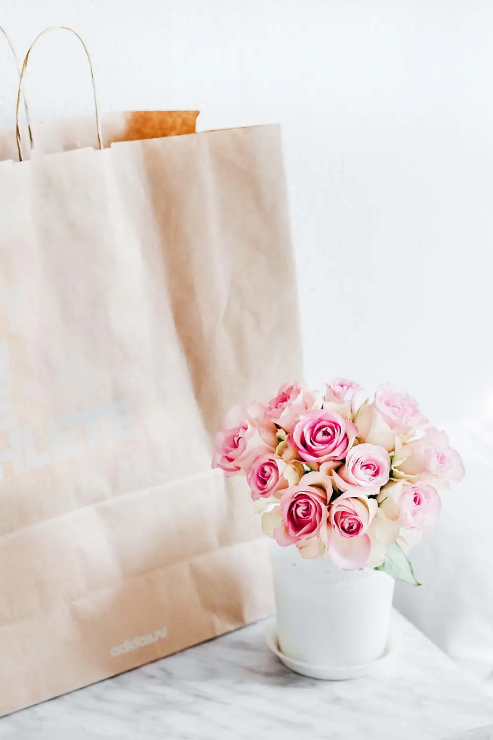 Brown shopping bag next to a vase of roses